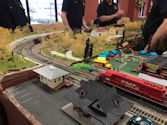 A model train crossing a river bridge, with a detailed forest landscape in the background.