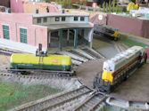A model train stopping at a rural train station with vintage-style buildings and waiting passengers.