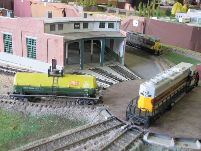 Model train turntable and roundhouse at the Oshawa Pine Ridge Model Railroaders Club, featuring locomotives and detailed rail yard scenery.
