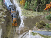 A diesel locomotive passing through a countryside setting with rolling hills and farms.