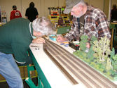 A model train traveling through a detailed mountain valley with a scenic background.