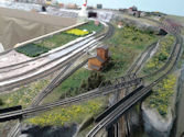 A classic steam locomotive traveling through a dense forested landscape with a bridge in the distance.