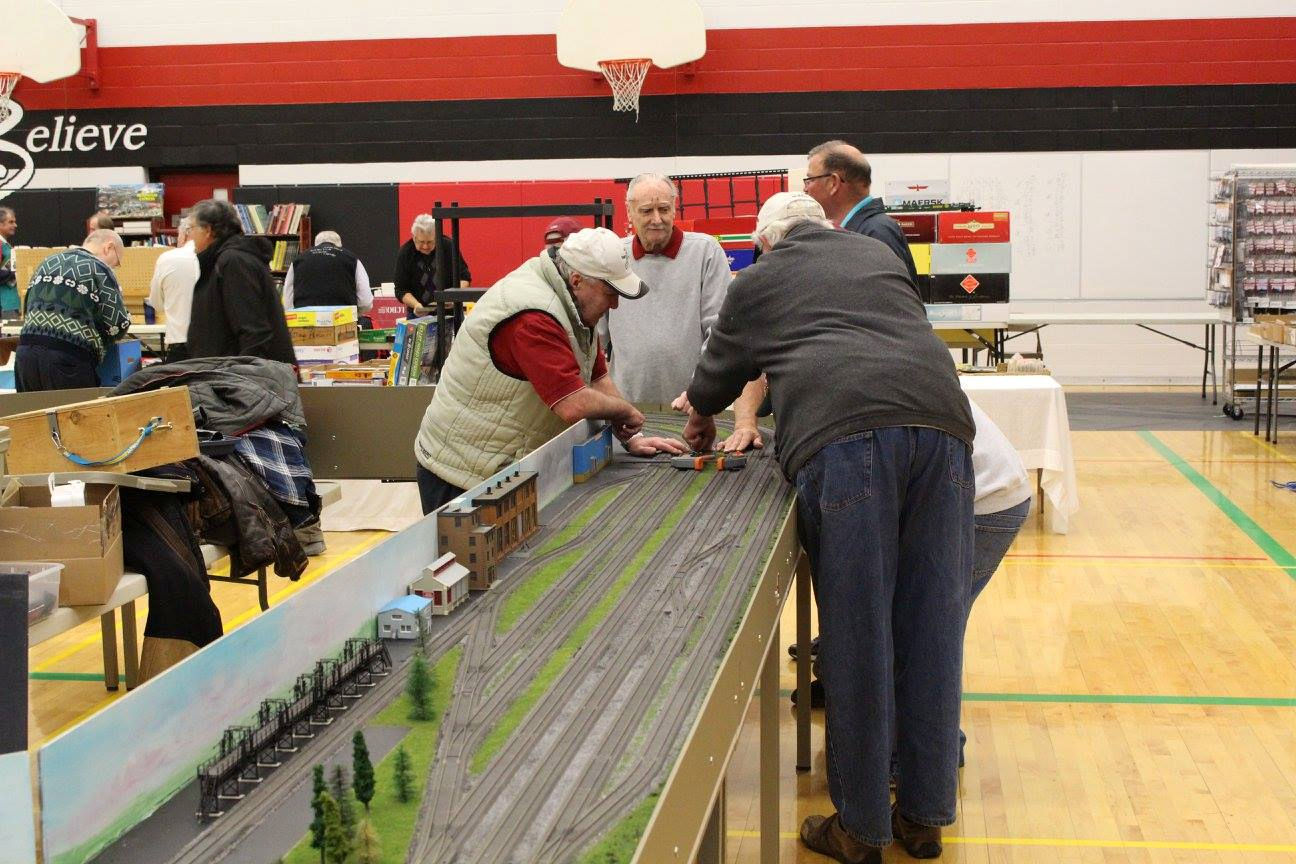 Model railroaders working on a detailed train yard layout at a model railway exhibition.