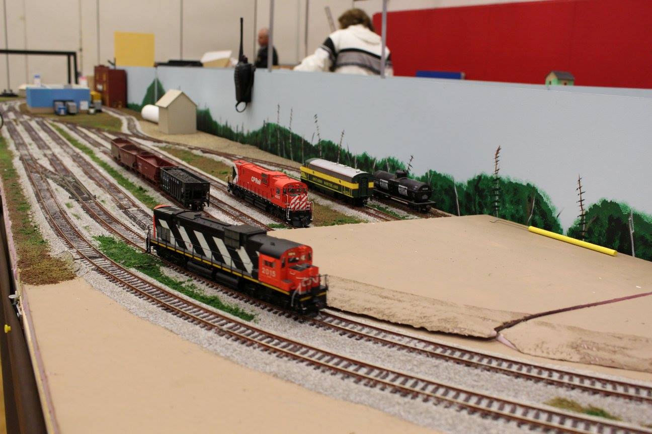 Model train yard with CP Rail and CN locomotives on display, complete with detailed scenery and multiple tracks.
