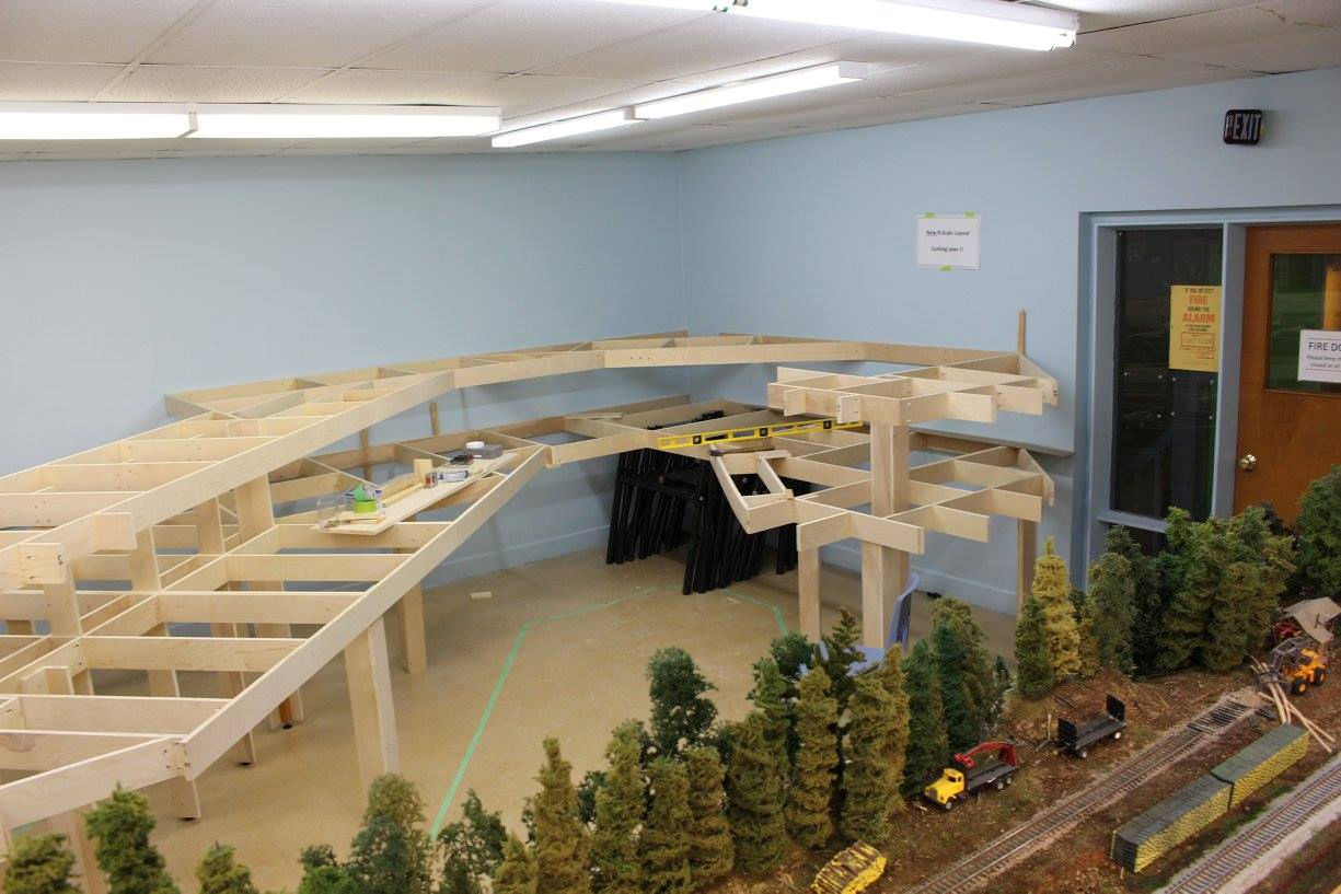 Model railroad framework under construction, with detailed scenery and train tracks in the foreground.