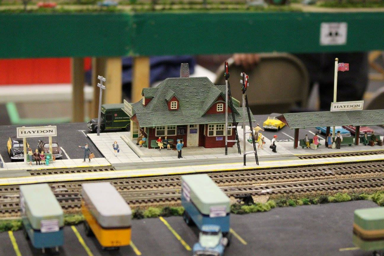 Miniature train station with passengers, vehicles, and railroad tracks.