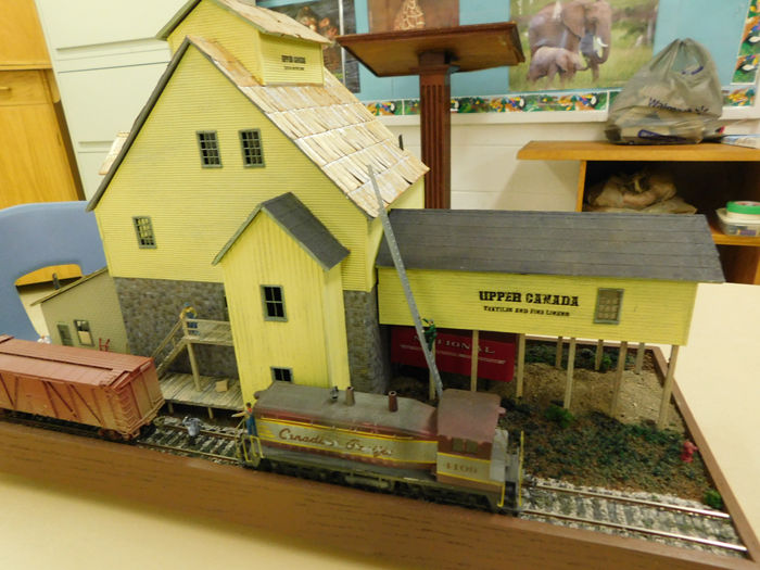 A yellow model train station with a grain elevator and a locomotive on the tracks.